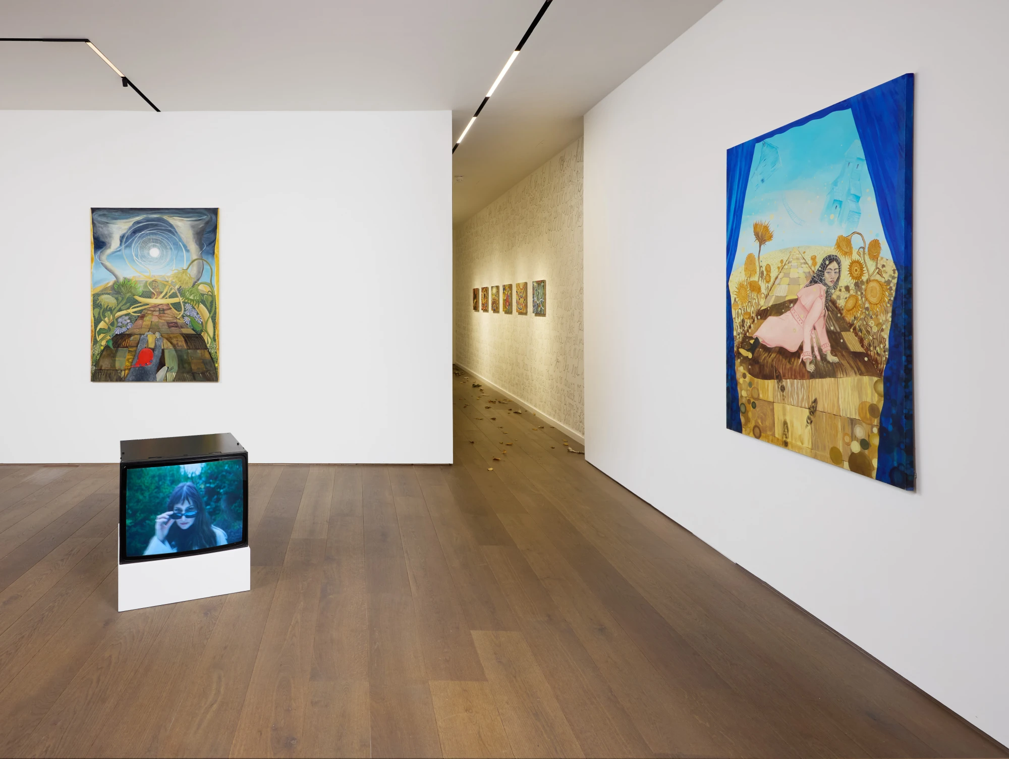 An installation shot of an art exhibition. There are two large paintings on the walls, and a block monitor on the floor. The hallway in the distance displays a series of six smaller scale paintings.