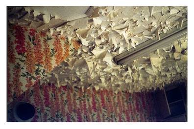 A collaged oil painting, the images are oriented in varying directions. It depicts a set of hands clasping red spotted flowers, a single lit white candle, a woman looking out onto a highway through veiled transparent curatins and a young girl at the table while her mother works in the kitcen behind her.